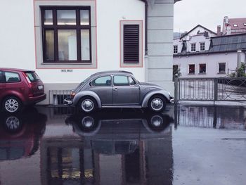 Vintage car parked against building on wet street in city during rainy season