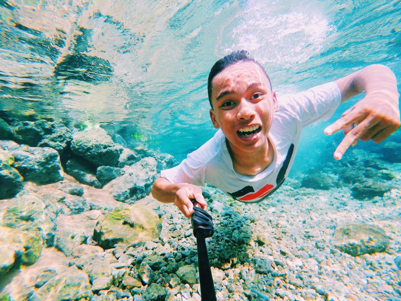 lifestyles, leisure activity, water, person, young adult, young men, portrait, looking at camera, shirtless, rock - object, vacations, blue, front view, casual clothing, standing, smiling, enjoyment, holding