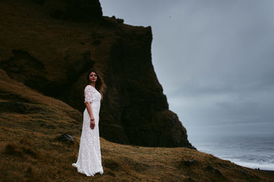 Woman standing on rock by sea against sky