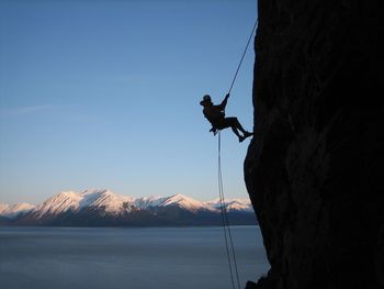 Man rock climbing on cliff against clear blue sky