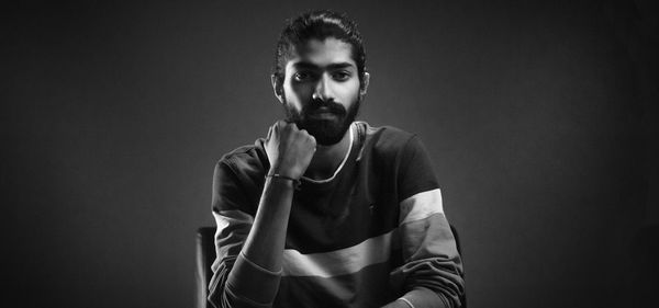 Portrait of young man standing against black background