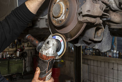 A mechanic grinds, with an angle grinder, the edge of an old rear brake disc in a car.