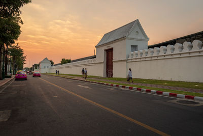 Road by buildings against sky during sunset in city