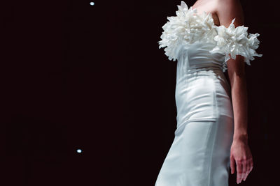 Elegant fashion details of white silky bridal dress. fashion model walking on black background