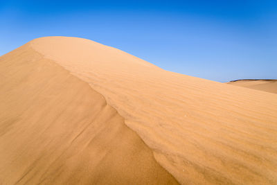 Sand dunes in desert against clear blue sky