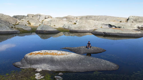 Man on rock by lake against sky