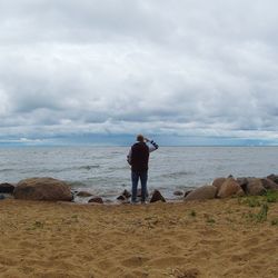 Rear view of man standing on beach against sky