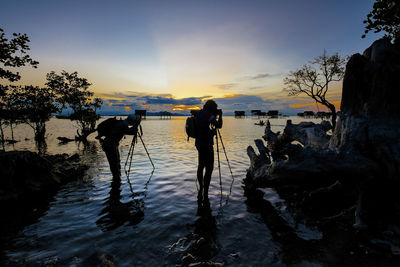 Silhouette man and woman photographing sea during sunset