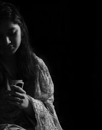 Close-up of young woman using smart phone against black background