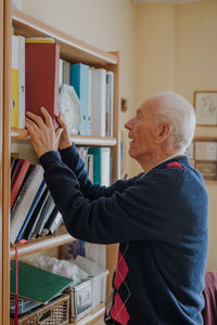 Senior man keeping book on shelf at home