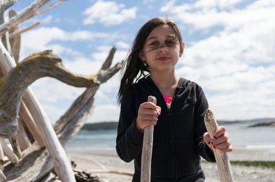 Portrait of girl holding wood while standing at beach