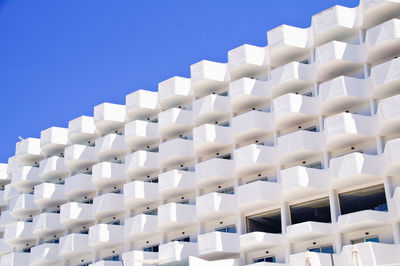 Low angle view of white balkony hotel building against blue sky