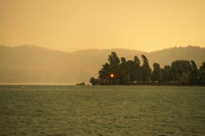 View of calm sea against mountain range in foggy weather