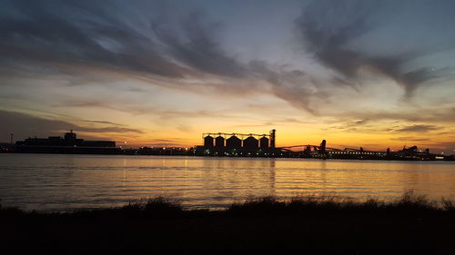 Silhouette of industry building by river at sunset