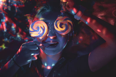 Close-up of woman holding lollipops while lying on bed in illuminated room