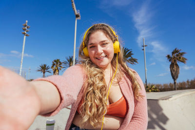 Portrait of smiling woman taking selfie against sky