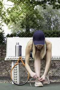 Unrecognizable woman sitting on a bench in the middle of a tennis match tying to laces of sneaker 