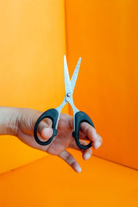 Midsection of man holding umbrella against orange wall