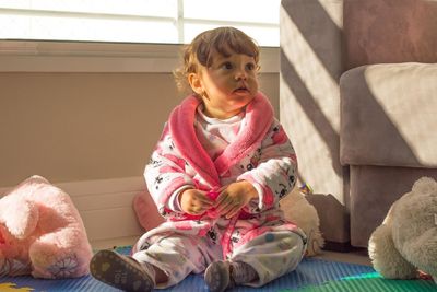 Girl looking away while sitting on pink indoors