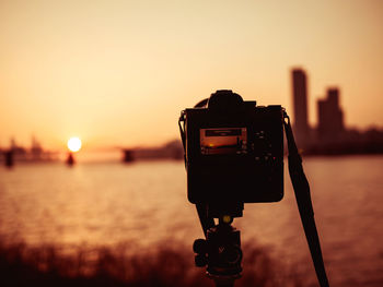 Close-up of camera against sky during sunset and bridge