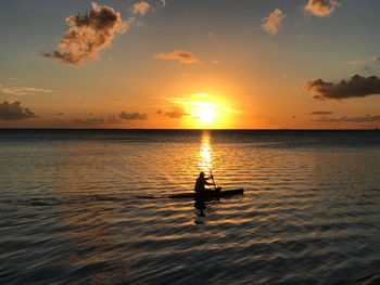 Silhouette man in sea against sky during sunset