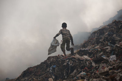 Full length of boy running on garbage dump against sky