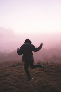 Rear view of man jumping on field during sunset