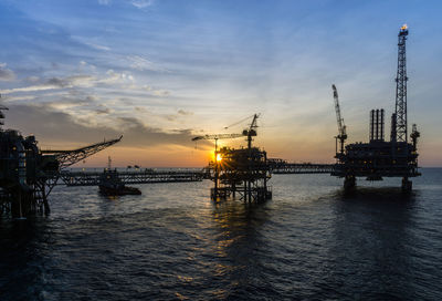 Silhouette cranes at commercial dock against sky during sunset