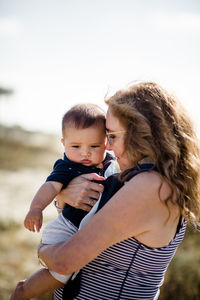 Grandmother holding & snuggling grandson while standing on beach