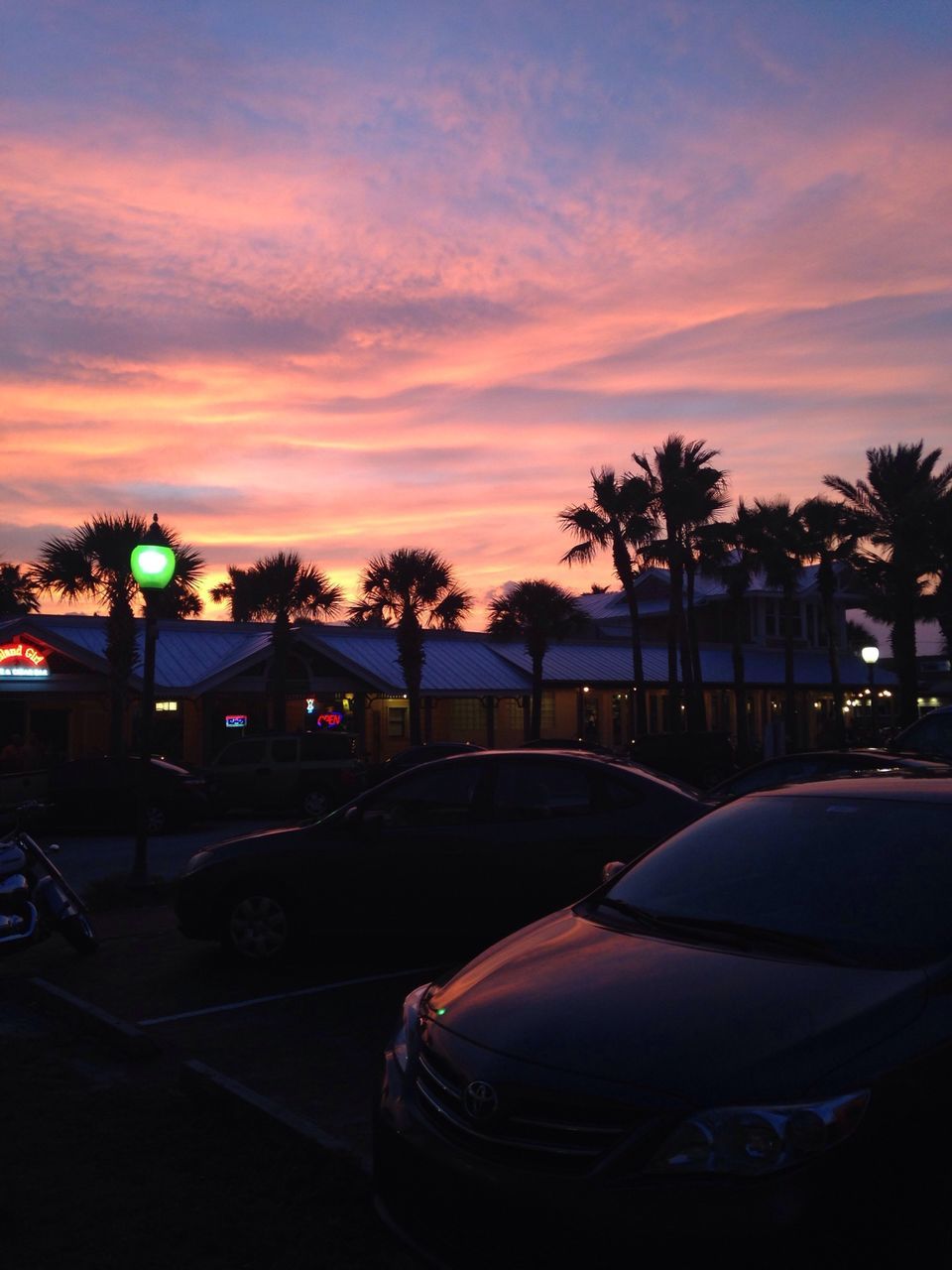 sunset, tree, sky, palm tree, transportation, silhouette, car, cloud - sky, mode of transport, illuminated, land vehicle, dusk, street light, cloud, street, nature, road, parking lot, outdoors, orange color