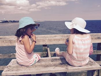 Sisters sitting on seat against sea