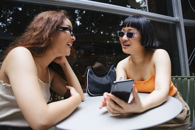 Smiling lesbian couple holding mobile phone while sitting at cafe