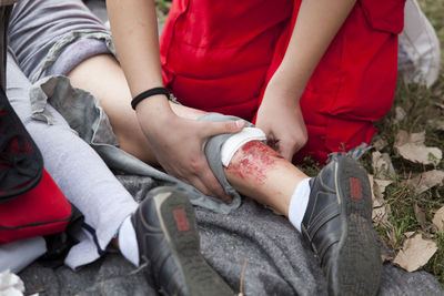 Low section of paramedic sitting by wounded woman on field