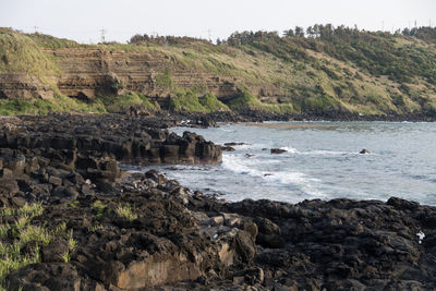 Scenic view of cliff by trees against sky