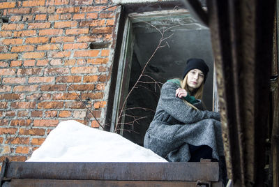 Portrait of woman sitting against brick wall