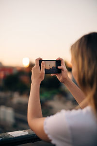 Cropped image of young woman photographing fernsehturm through smart phone during sunset