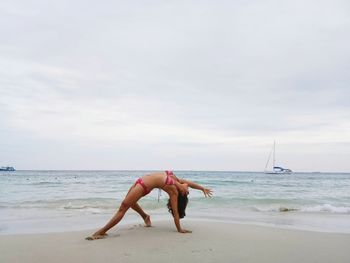 Woman in bikini stretching at beach against sky