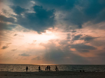 Silhouette people on beach against sky during sunset