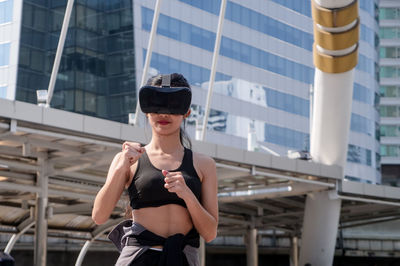 Woman wearing 3-d glasses while gesturing against building