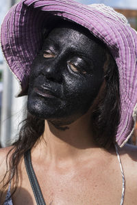 Caucasian woman with face made up in black color. she is wearing a pink colored hat. 