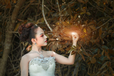 Young woman wearing dress touching leaves in park