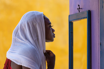 African ghana woman standing in front of a mirror with a white shawl covering her hair