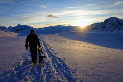 Rear view of man in snow against sky during sunset