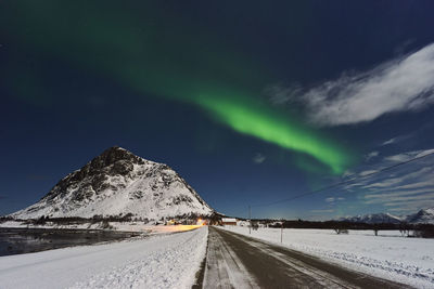 Road amidst snowcapped mountains against sky at night