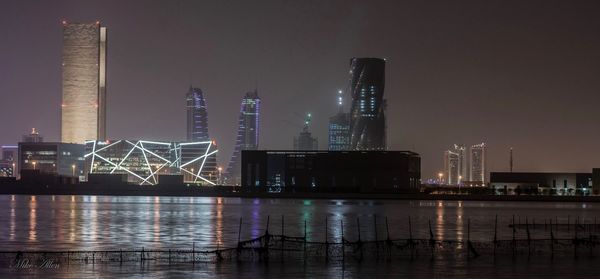 Illuminated city by river against sky at night
