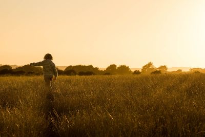 Girl walking on field against sky during sunset