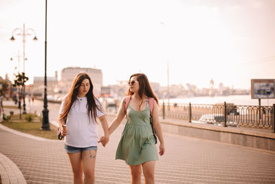 Lesbian couple talking while walking in city holding hands in summer