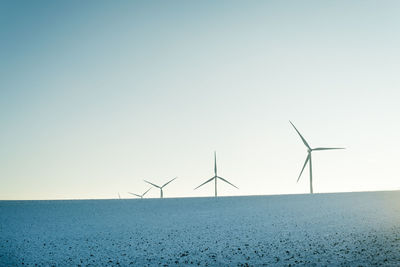 Wind turbines on field against clear sky