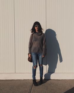 Full length portrait of young woman standing against wall