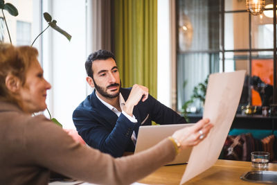 Confident male and female professionals discussing over drawing on paper at table in office